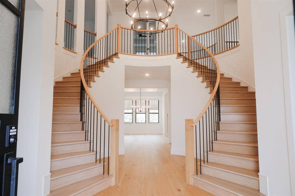 10694 Hollydale Lane, Frisco, TX 75035 Grand dual-staircase foyer featuring wood-finish treads, metal balusters, polished wood handrails, and a large multi-tiered iron chandelier