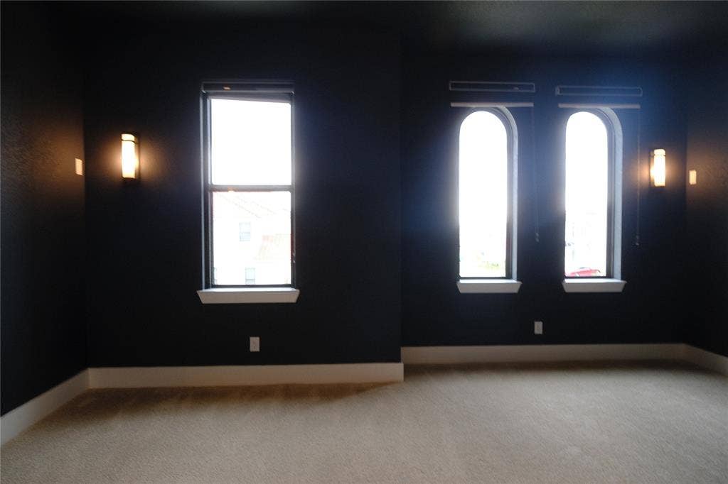 10694 Hollydale Lane, Frisco, TX 75035 Media room featuring high-contrast wall and ceiling paint, wall-mounted light fixtures, arched windows with integrated blinds, and wall-to-wall carpeting
