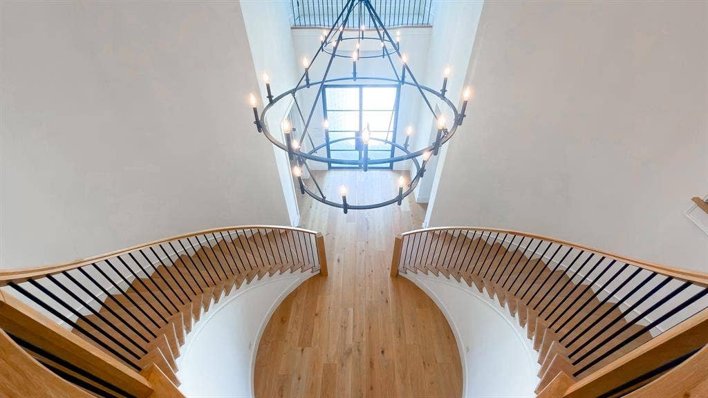 10694 Hollydale Lane, Frisco, TX 75035 Double curved staircase with wood treads and handrails featuring thin black metal balusters, large metal multi-tier chandelier, and wood-finish flooring
