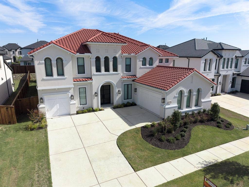 10694 Hollydale Lane, Frisco, TX 75035 Two-story stucco exterior featuring a red tile roof, arched windows, covered entryway, and an attached three-car garage