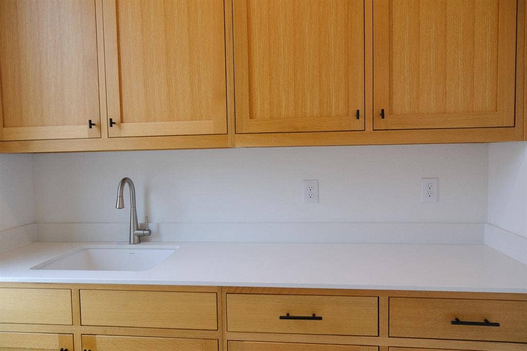 10694 Hollydale Lane, Frisco, TX 75035 Laundry Room Sink, Light-toned wood cabinetry, clean-lined white stone countertops, an integrated white undermount sink, a sleek stainless steel gooseneck faucet, and matte black hardware
