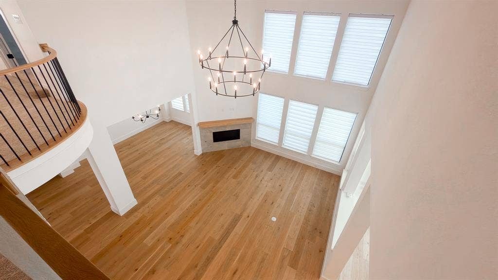 10694 Hollydale Lane, Frisco, TX 75035 Double-height ceiling, wood-finish flooring, stone-surround fireplace with a wood mantel, multi-tier metal chandelier, and curved balcony with a metal railing