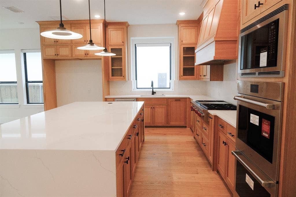 10694 Hollydale Lane, Frisco, TX 75035 Kitchen featuring custom light wood cabinetry, white stone-surface countertops, a large center island, stainless steel wall-mounted oven and microwave, and wood-finish flooring