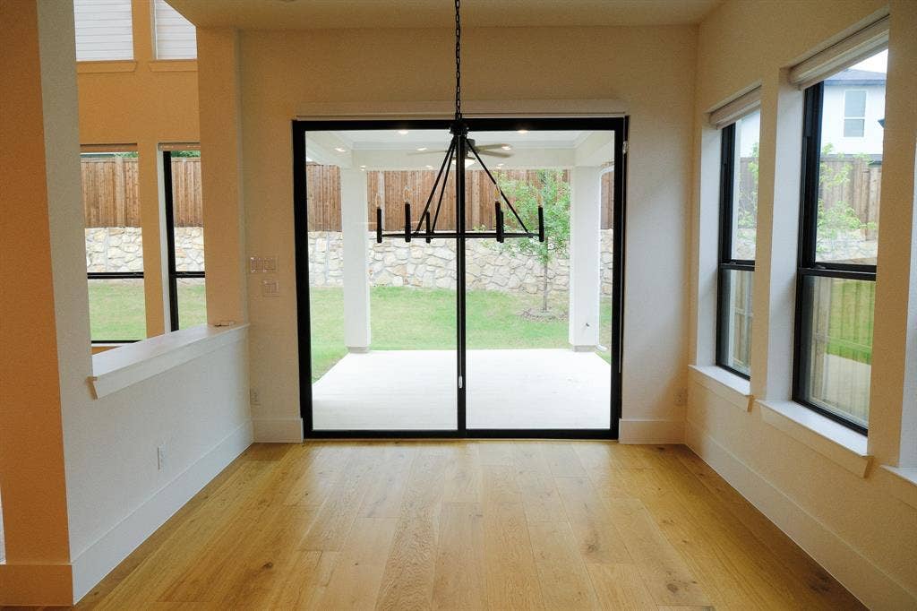 10694 Hollydale Lane, Frisco, TX 75035 Wood-finish flooring, matte black multi-pane windows, sliding glass door, and geometric metal chandelier