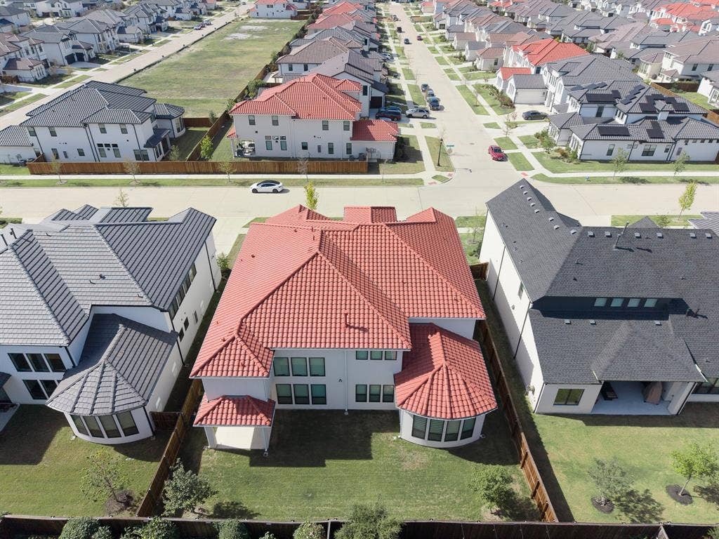 10694 Hollydale Lane, Frisco, TX 75035 Two-story residence featuring a terracotta-style tile roof, stucco exterior, rear curved architectural bay, fenced backyard, and a covered patio