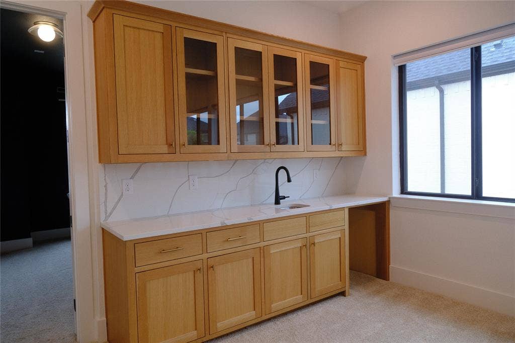 10694 Hollydale Lane, Frisco, TX 75035 Custom cabinetry featuring glass-front upper doors, stone-finish countertops, full-height decorative backsplash, integrated sink with matte black faucet, and built-in workspace