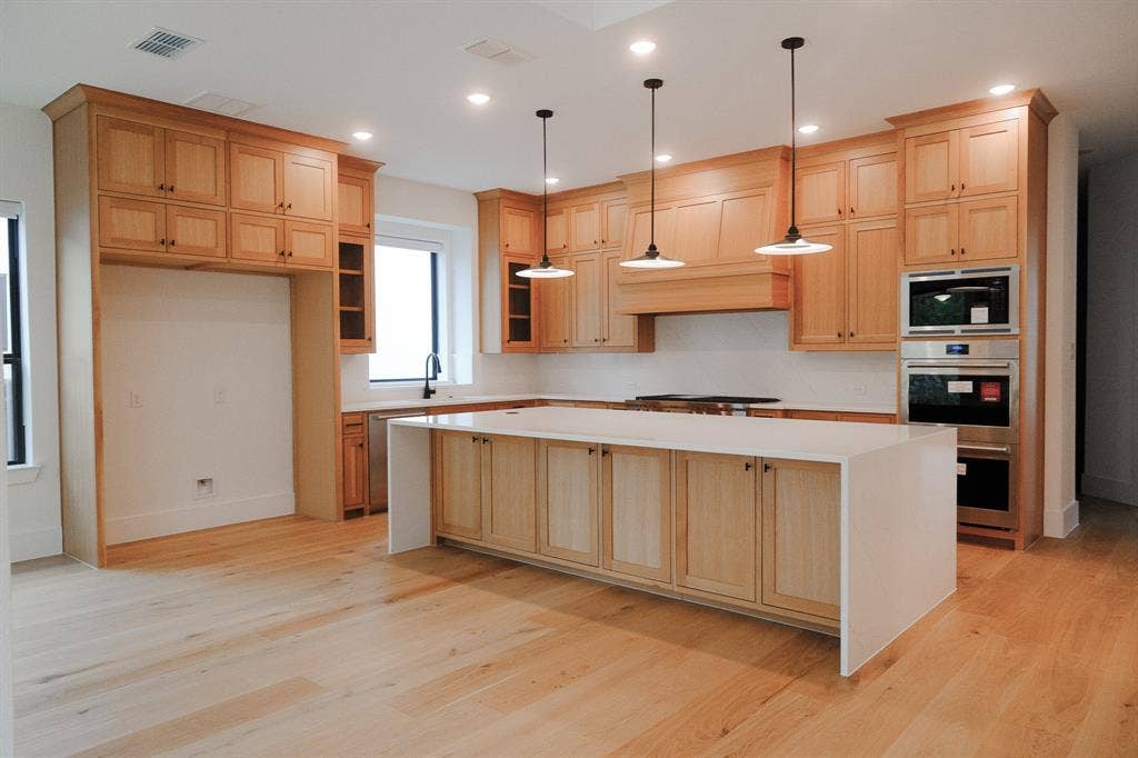 10694 Hollydale Lane, Frisco, TX 75035 Kitchen featuring light wood cabinetry, a central island with a waterfall countertop, integrated stainless steel appliances, and pendant lighting