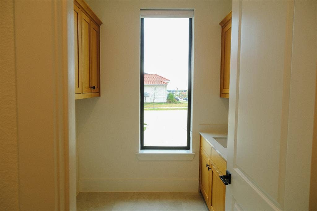 10694 Hollydale Lane, Frisco, TX 75035 Laundry Room vertical window, wood-finish cabinetry, stone countertop with integrated sink, and matte black hardware