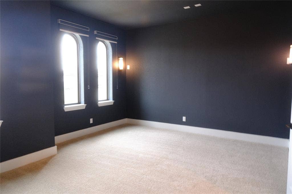 10694 Hollydale Lane, Frisco, TX 75035 Media room featuring high-contrast wall and ceiling paint, wall-mounted light fixtures, arched windows with integrated blinds, and wall-to-wall carpeting