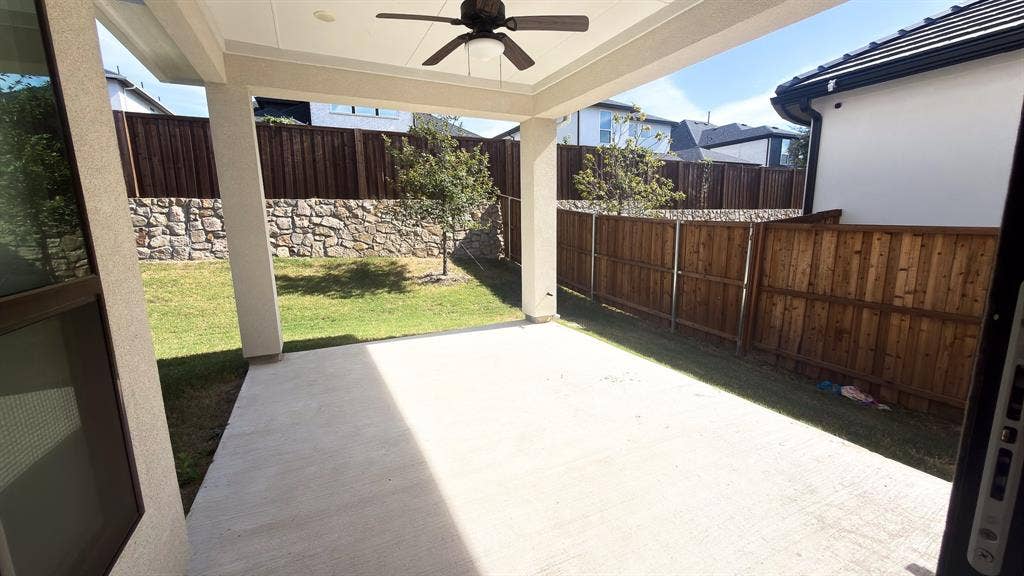 10694 Hollydale Lane, Frisco, TX 75035 Covered concrete patio featuring a ceiling fan, privacy wood fencing, and stone retaining wall