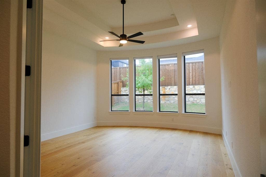 10694 Hollydale Lane, Frisco, TX 75035 Master Bed Room featuring wood-finish flooring, a tiered tray ceiling, four floor-to-ceiling windows, and a central ceiling fan