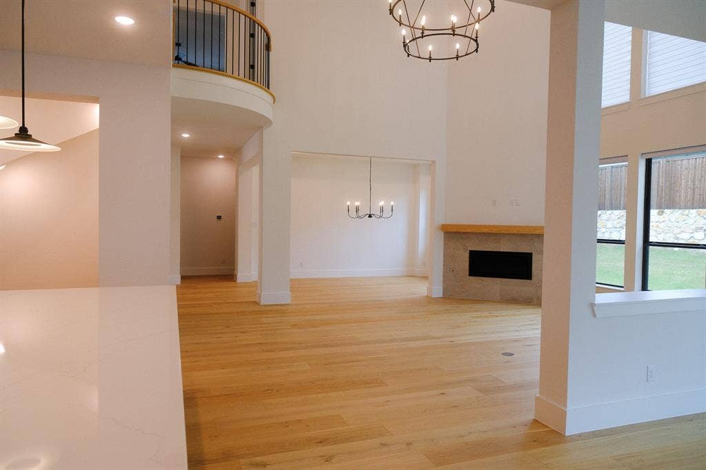 10694 Hollydale Lane, Frisco, TX 75035 Two-story ceiling height, light-toned wood-finish flooring, fireplace with stone surround and wood mantel, iron chandelier lighting, and a curved balcony with iron railing