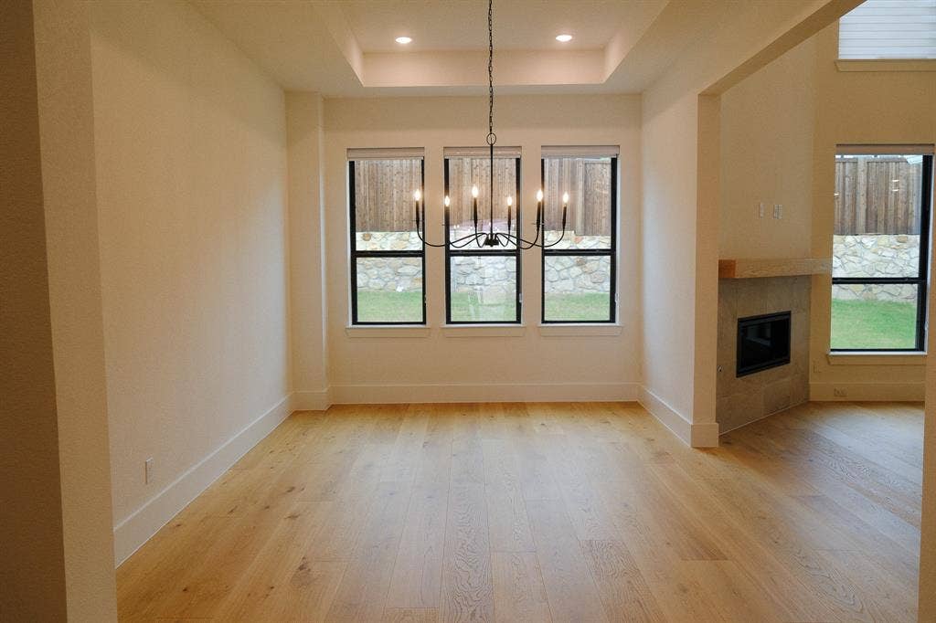 10694 Hollydale Lane, Frisco, TX 75035 Dining area featuring wood-finish flooring, a tray ceiling with recessed lighting, a multi-arm chandelier, and a fireplace with a stone surround and timber mantel