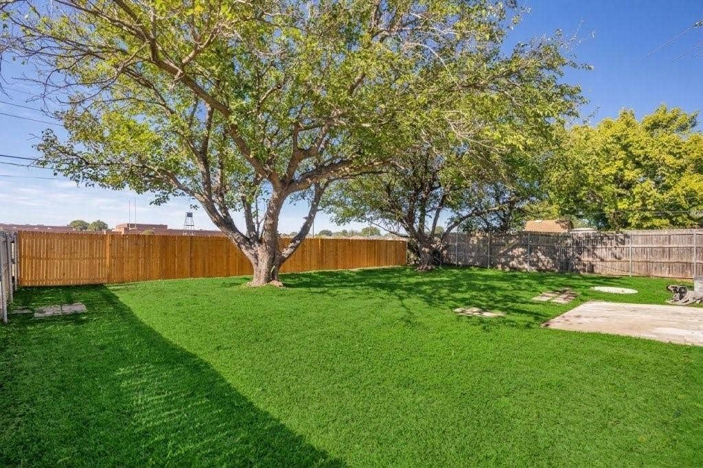 Expansive backyard featuring mature shade trees, a manicured lawn, and perimeter wood fencing