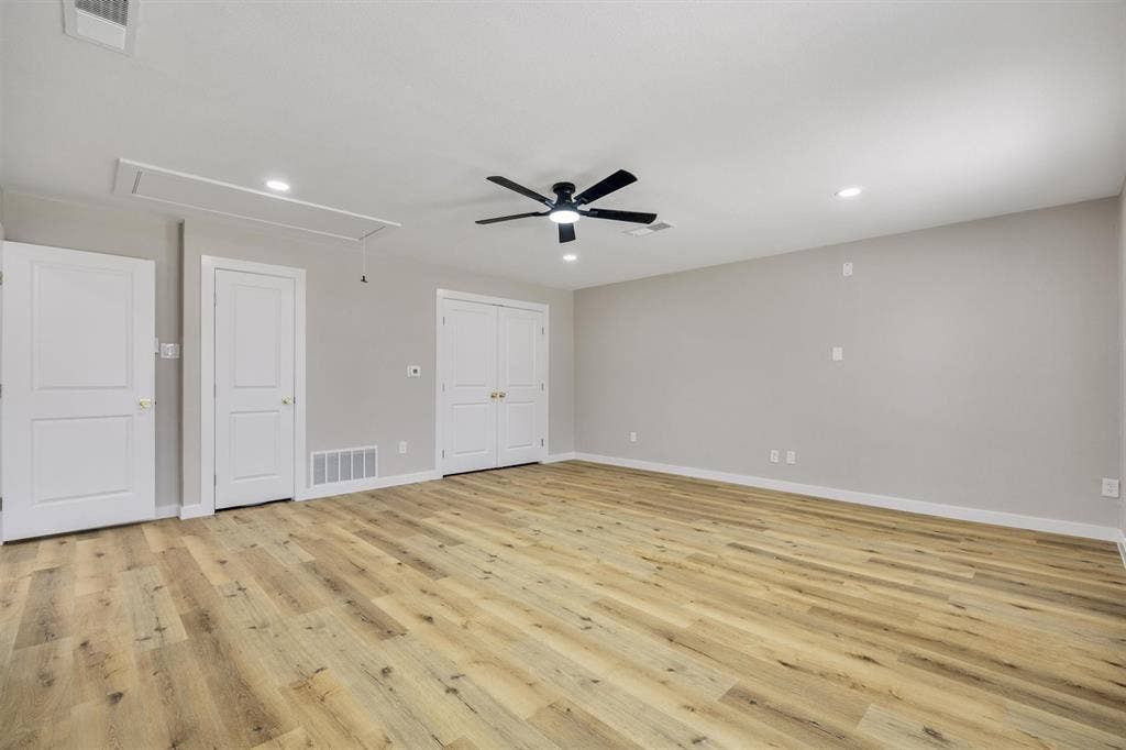 Spacious room featuring wood-finish flooring, recessed lighting, and a central ceiling fan with an integrated light fixture