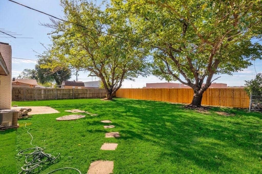Expansive backyard featuring a level lawn, mature trees, wood privacy fencing, and concrete hardscaping