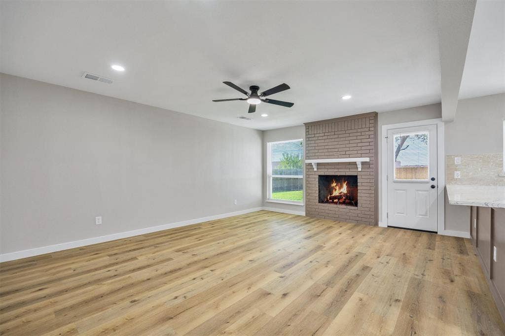 Living area featuring wood-finish flooring, brick fireplace with mantel, recessed lighting, ceiling fan, and exterior access door