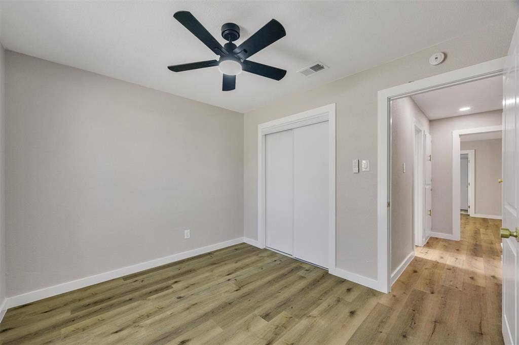 Room featuring wood-finish flooring, a five-blade ceiling fan with integrated lighting, and a closet with sliding doors