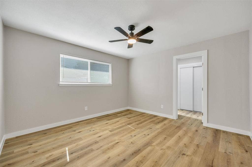 Neutral-toned walls, wood-finish flooring, ceiling-mounted light fixture with fan, and sliding closet doors