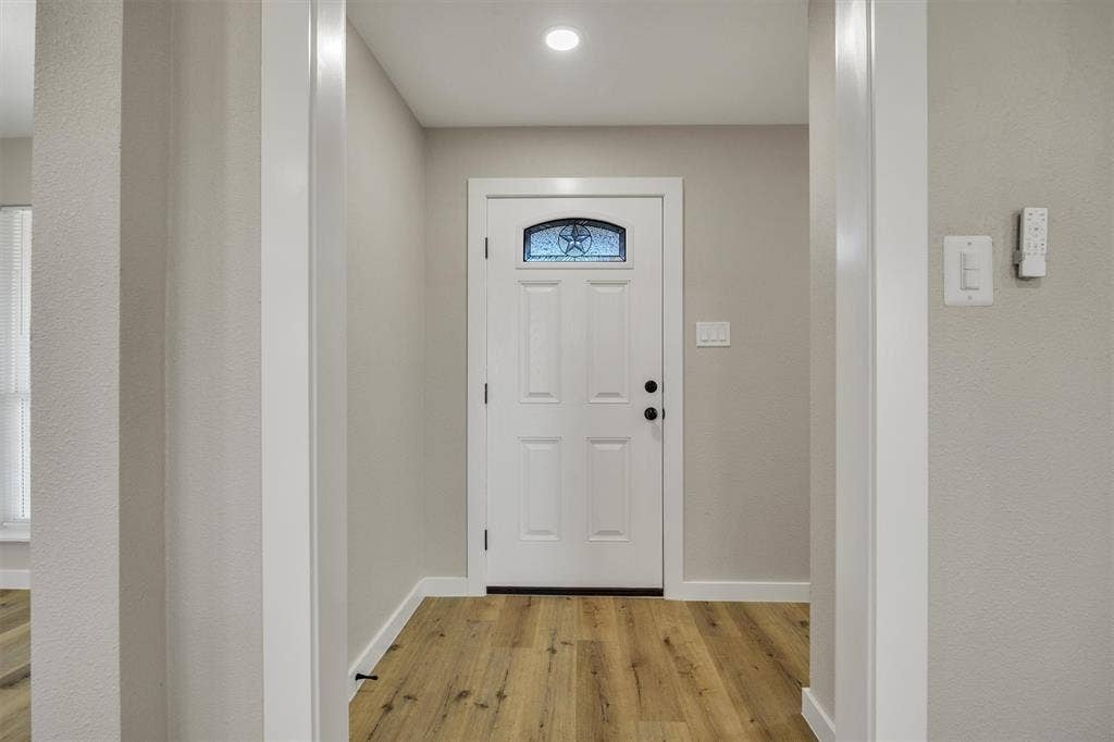 Entryway featuring wood-finish flooring, a white paneled front door with a decorative arched window insert, and recessed ceiling lighting