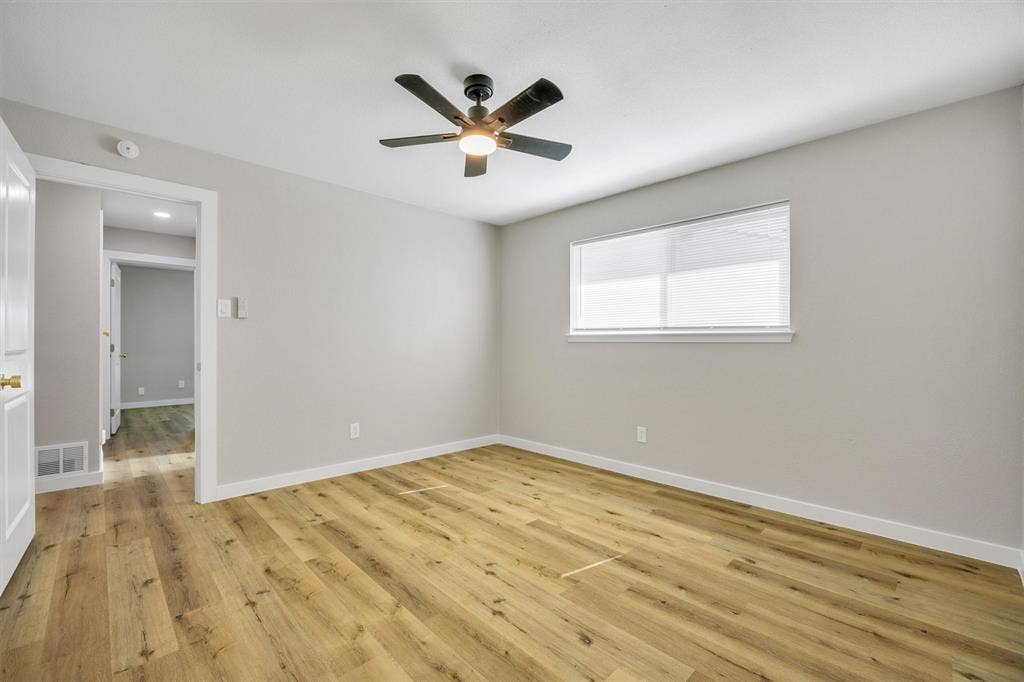 Neutral interior room featuring wood-finish flooring, a matte black ceiling fan with integrated lighting, and a horizontal sliding window