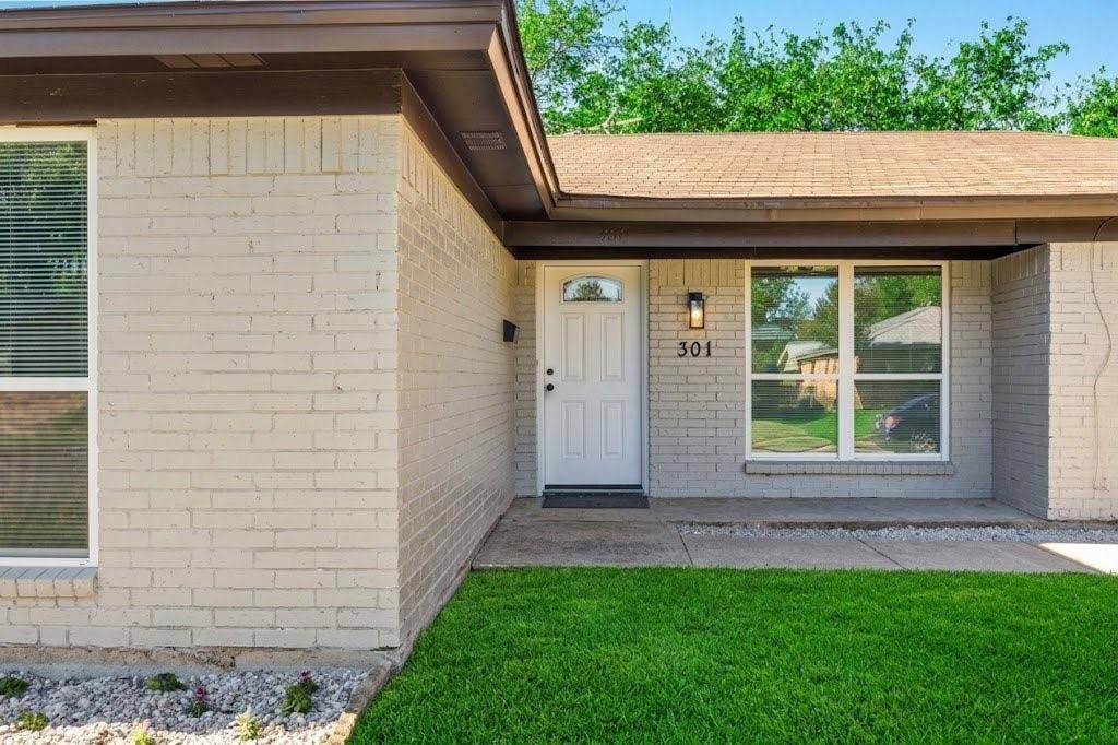 Exterior facade featuring painted brick, a composite shingle roof, a concrete walkway, and an arched-top entry door