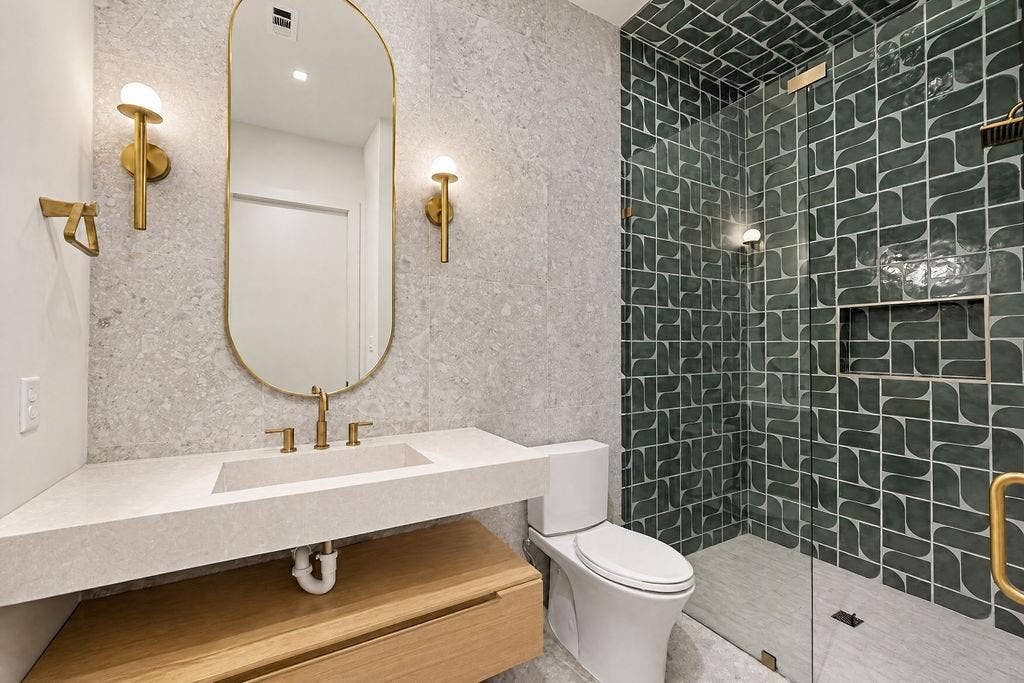 This main floor bath is detailed with green shower tile, a floating vanity, and a warm rounded mirror