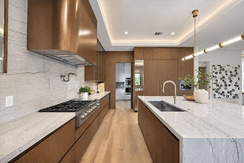 Craft favorite meals on the gas cooktop under a striking custom hood, surrounded by stunning finishes and smart storage drawers