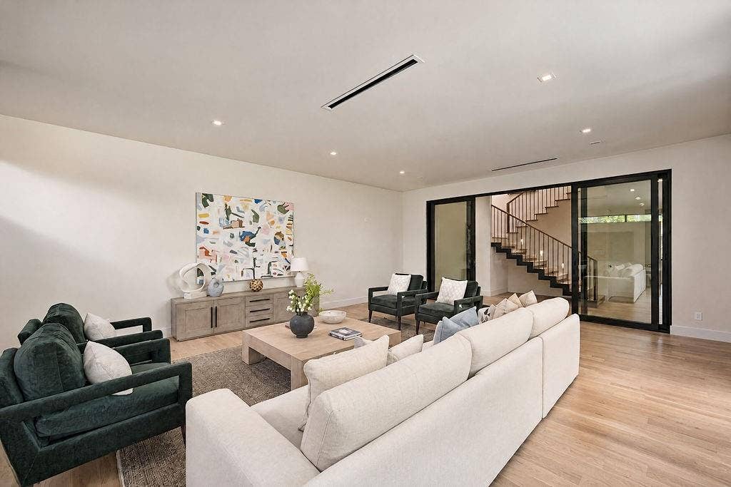Lounging here feels grounded and effortless, framed by soft architectural ceiling lights and the dramatic backdrop of the floating wood stairs