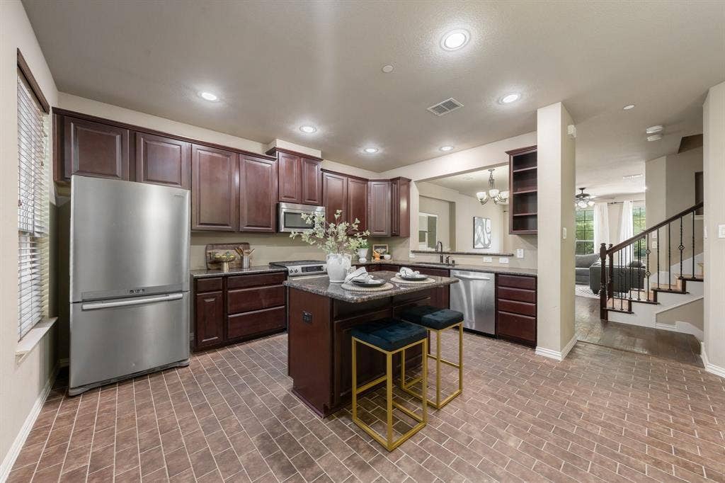 Kitchen featuring dark wood cabinetry, a central island with stone-finish countertop, stainless steel appliances, and tile flooring