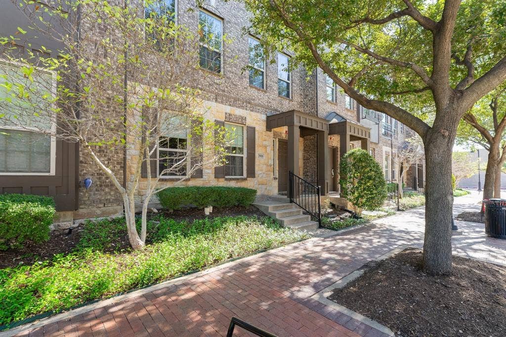 Multi-story exterior featuring a brick and stone facade, dark-toned shutters, covered entryway, and red brick pedestrian walkway