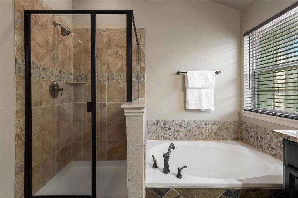 Walk-in shower with a black-framed glass enclosure, deep soaking tub, tile surround with decorative mosaic accents, and oil-rubbed bronze fixtures