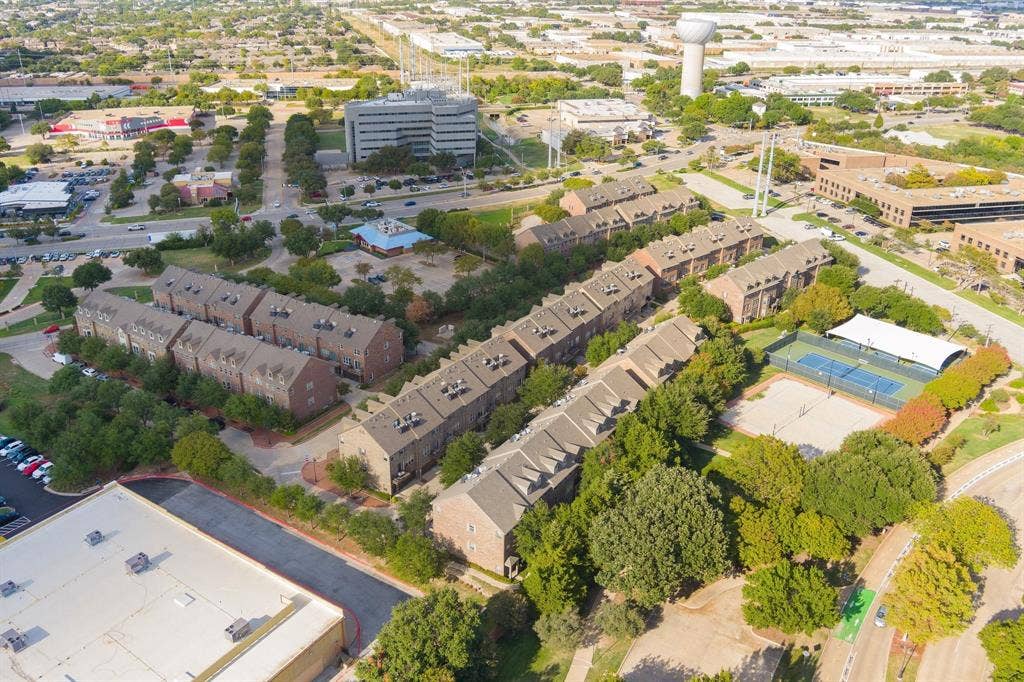 Aerial view of multi-story brick residential structures including a fenced tennis court and recreational area within the property grounds