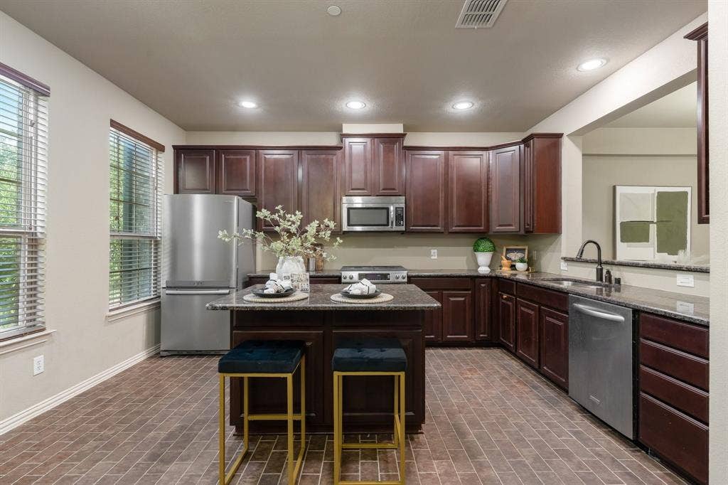 Kitchen featuring dark wood cabinetry, a central island with a stone countertop, recessed lighting, stainless steel appliances, and brick-style flooring