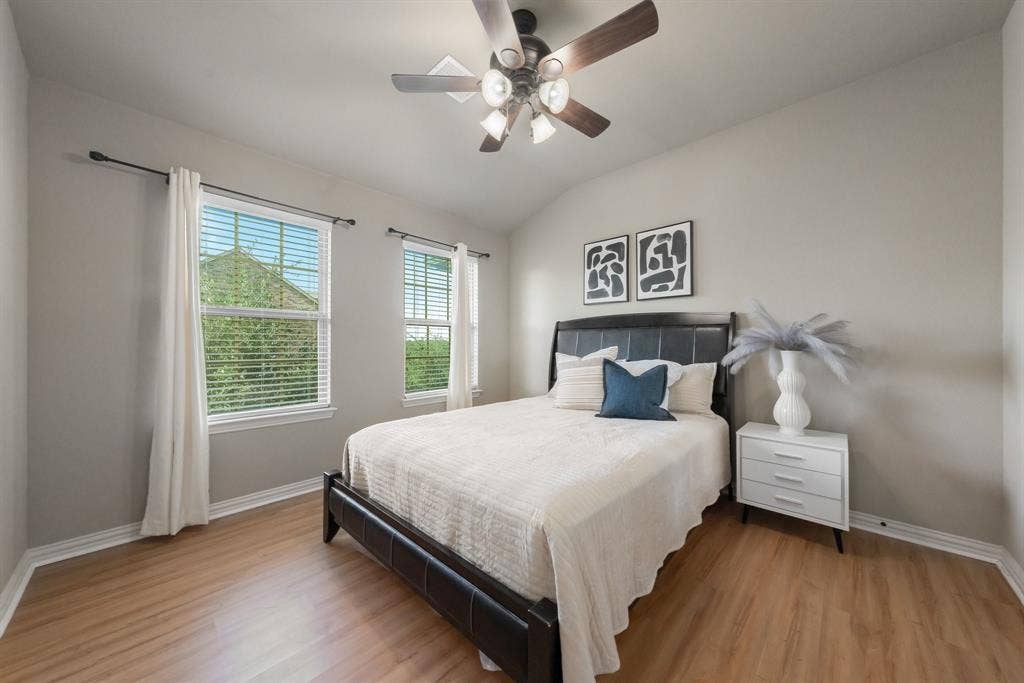 Neutral interior featuring wood-finish flooring, vaulted ceilings, dual-pane windows with blinds, and a multi-light ceiling fan