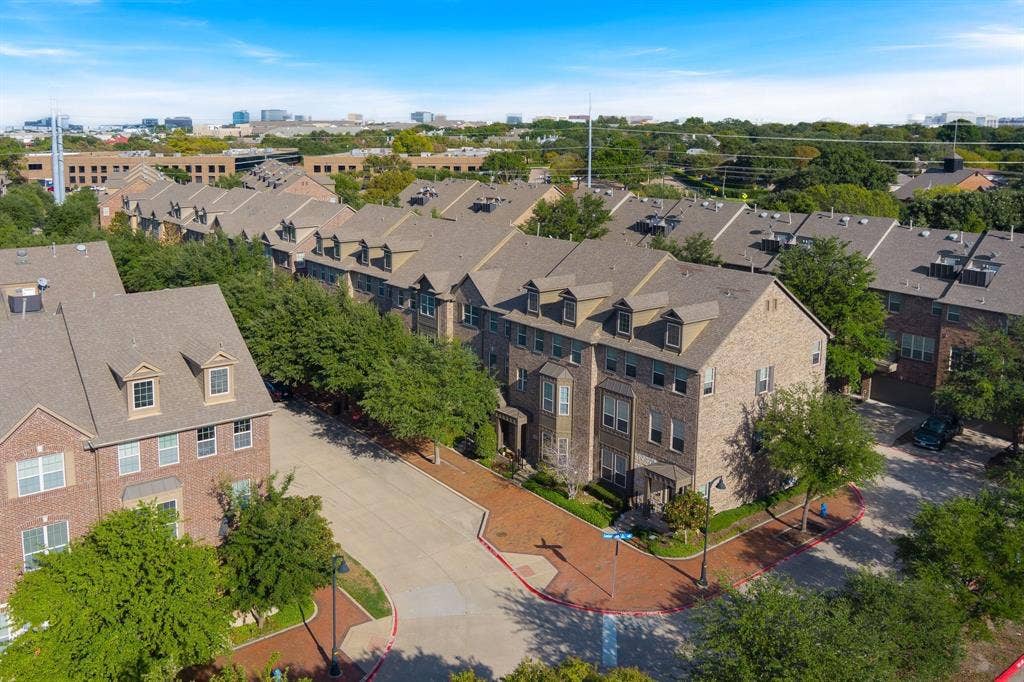 Multi-story brick facade townhome complex featuring peaked dormer windows, shingled roofing, and paved brick walkways throughout the grounds