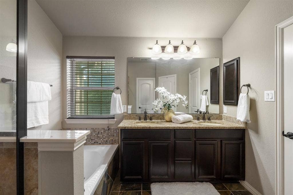 Double vanity with dark wood-finish cabinetry, stone-style countertops, integrated dual sinks, and a large wall-mounted mirror