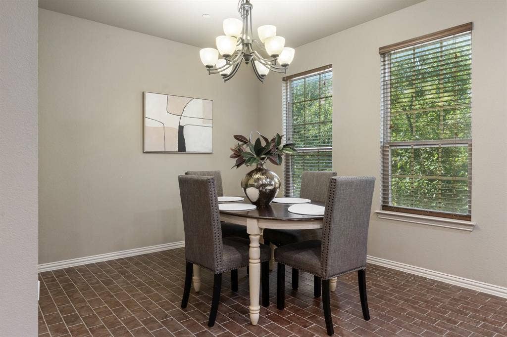 Dining area featuring brick-style tile flooring, multi-light chandelier with glass shades, and two windows with slatted blinds