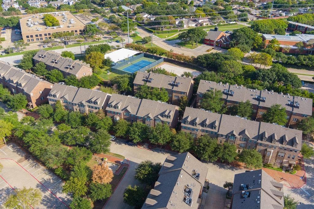 Aerial perspective of a multi-unit residential community featuring brick masonry exteriors, pitched shingle roofing, mature tree canopy, and paved surface parking