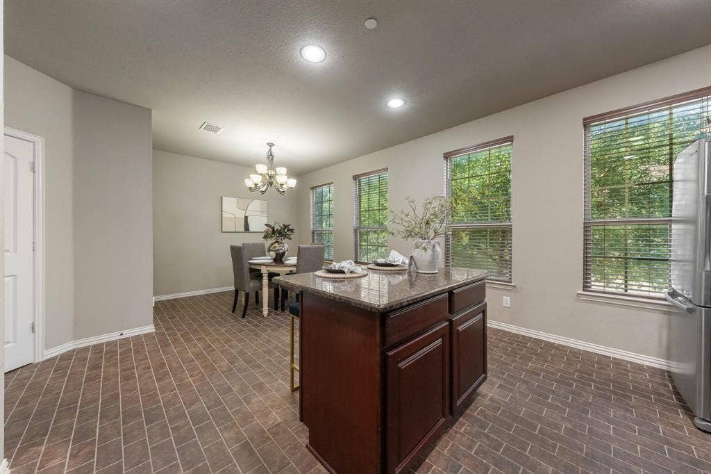 Kitchen island featuring a stone countertop and dark wood cabinetry, brick-style tile flooring, recessed lighting, and multiple large windows