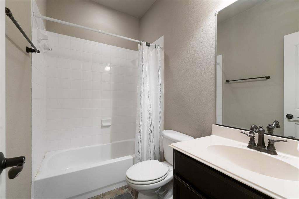 Bathroom featuring a dark wood-finish vanity, integrated oval sink, oil-rubbed bronze faucet, and a porcelain tub-shower combination with full-height tile surround