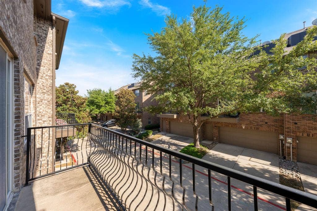 Private balcony featuring a black metal railing and concrete flooring overlooking brick exterior masonry and mature landscaping