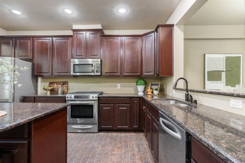 Kitchen featuring dark wood-finish cabinetry, stone-finish countertops, stainless steel appliances, a double-basin sink with a high-arch faucet, and tile flooring