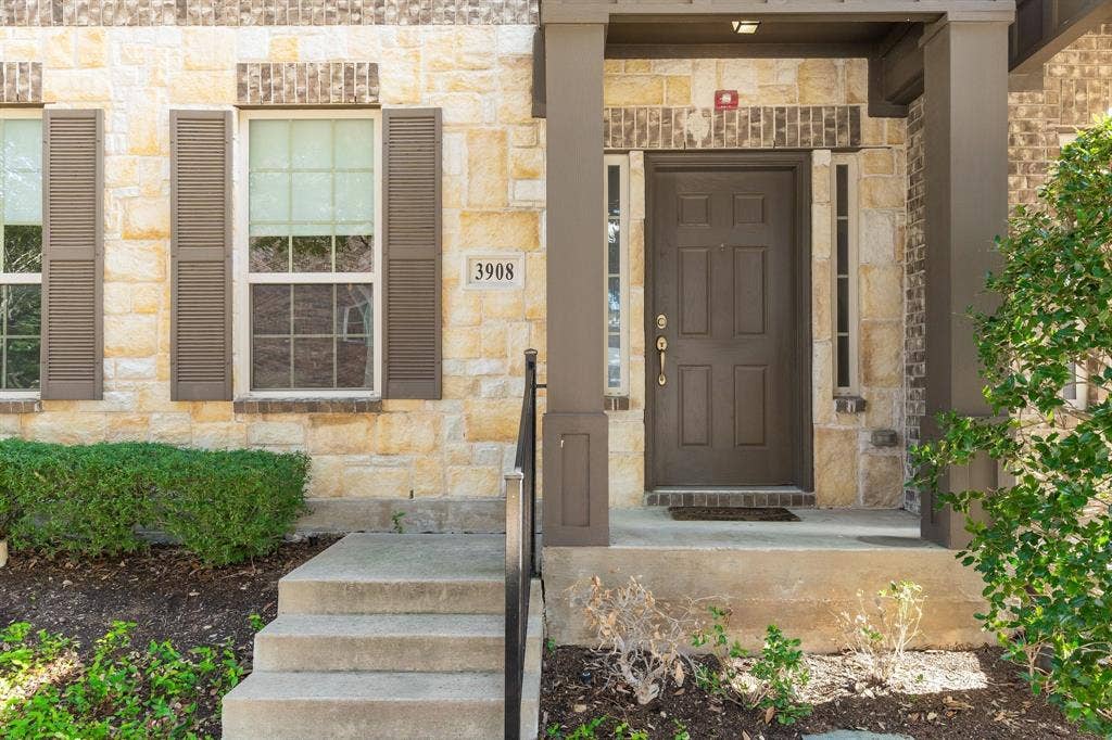 Stone veneer exterior with dark-toned shutters, covered entryway, concrete steps with metal railing, and multi-pane windows