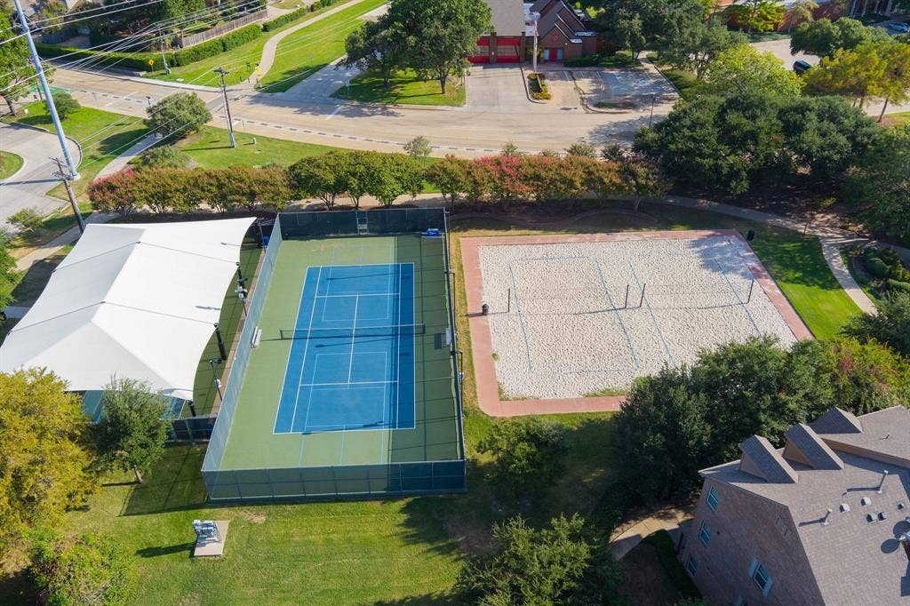 Fenced tennis court with a tension-fabric shade structure and sand volleyball court