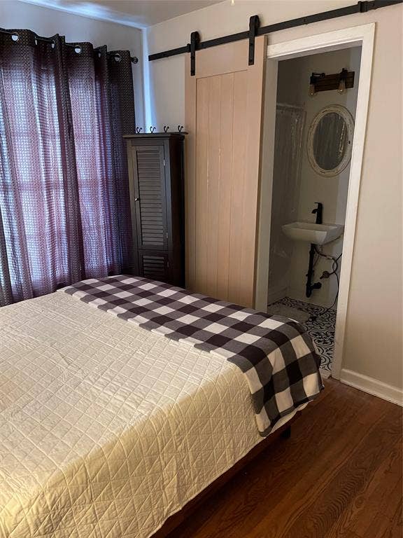 Light-toned wood barn door, wood-finish flooring, patterned tile flooring in bathroom, wall-mounted sink, and oval mirror