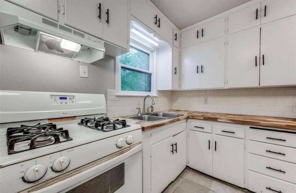 Kitchen featuring white cabinetry with matte black hardware, wood-finish countertops, subway tile backsplash, and a double-basin stainless steel sink with a pull-down faucet