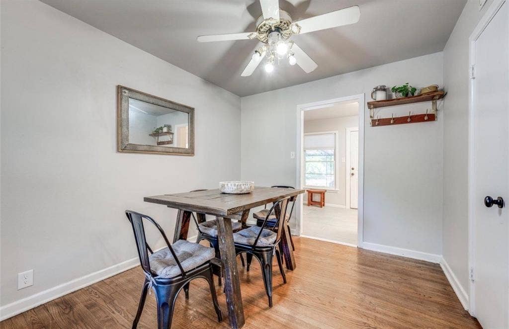 Neutral interior featuring wood-finish flooring, a ceiling-mounted fan with integrated light fixtures, and a wall-mounted wooden shelf with metal hooks