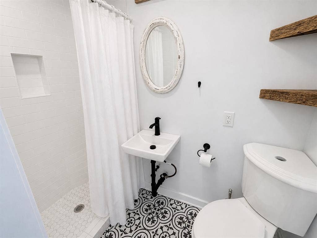 Bathroom featuring patterned floor tile, wall-mounted sink with matte black faucet, shower with integrated wall niche, and natural wood-finish floating shelving