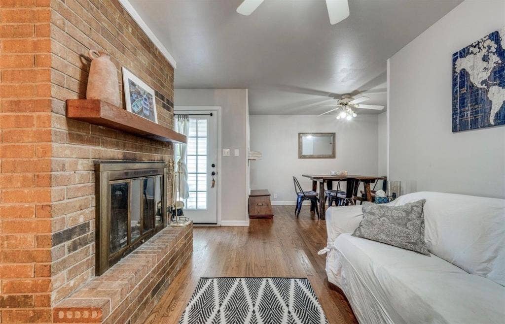 Brick fireplace featuring a wooden mantel and a glass-paneled insert, complemented by wood-finish flooring, ceiling fans, and a glass-paneled exterior door
